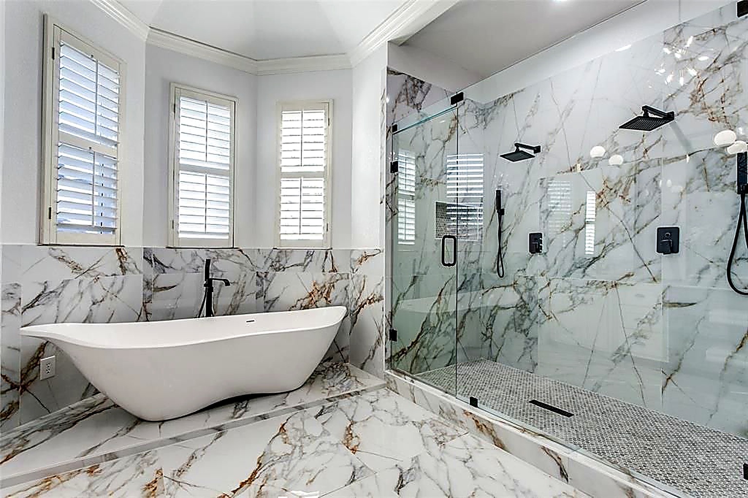 Freestanding soaking tub and frameless glass walk-in shower with marble surround
