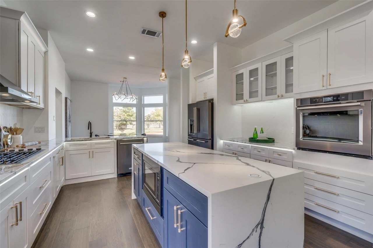 Full kitchen renovation with white shaker cabinets, navy island, waterfall quartz countertop, and gold pendant lighting