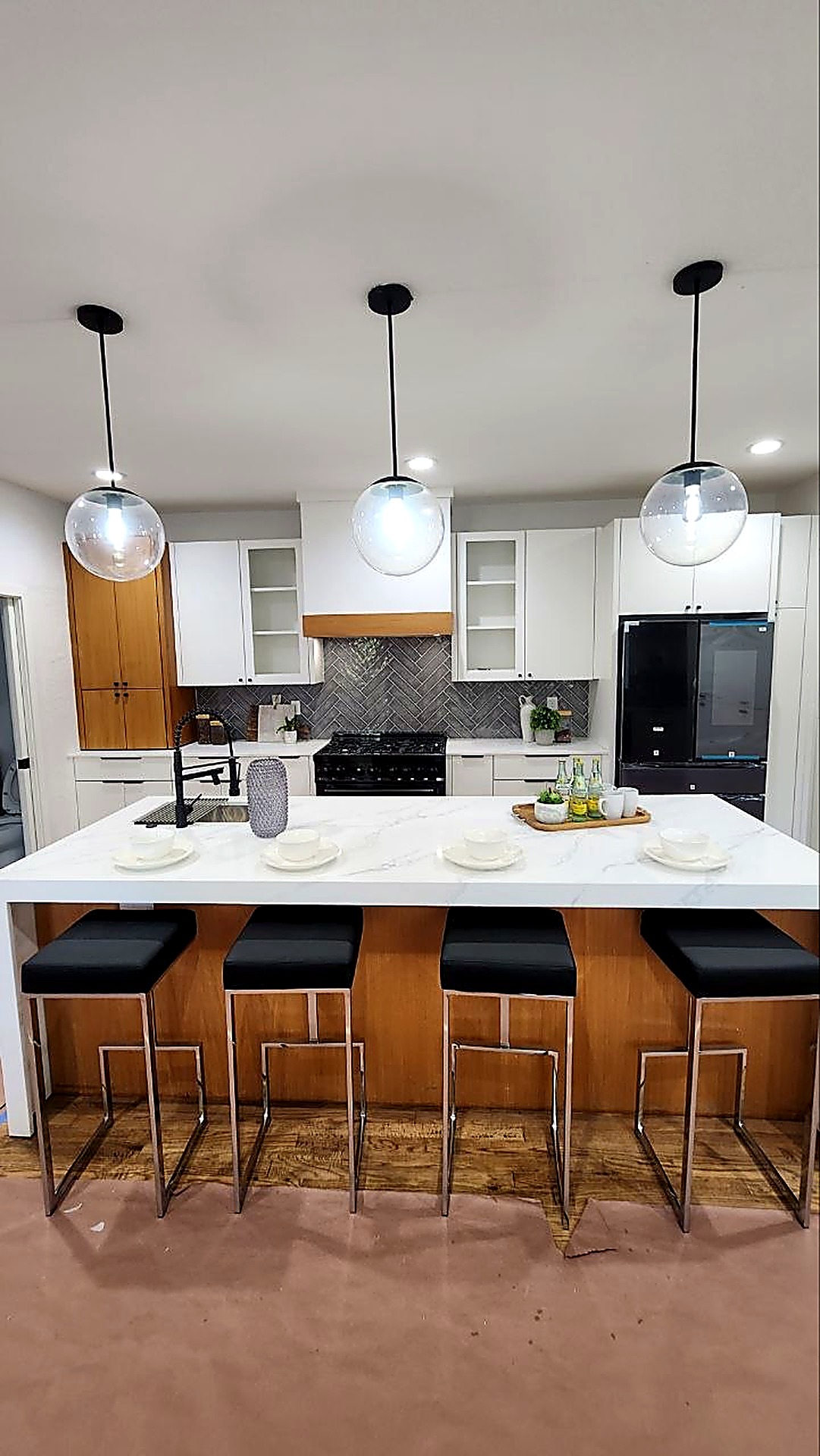 Kitchen island with waterfall quartz countertop, glass globe pendant lighting, and herringbone tile backsplash